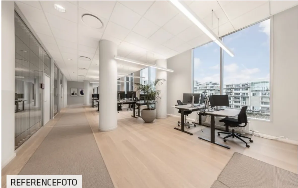 Moderne kontor med højloft, glasvægge, trægulv, lysekroner og skriveborde med plante og computere, udsigt til bygninger og