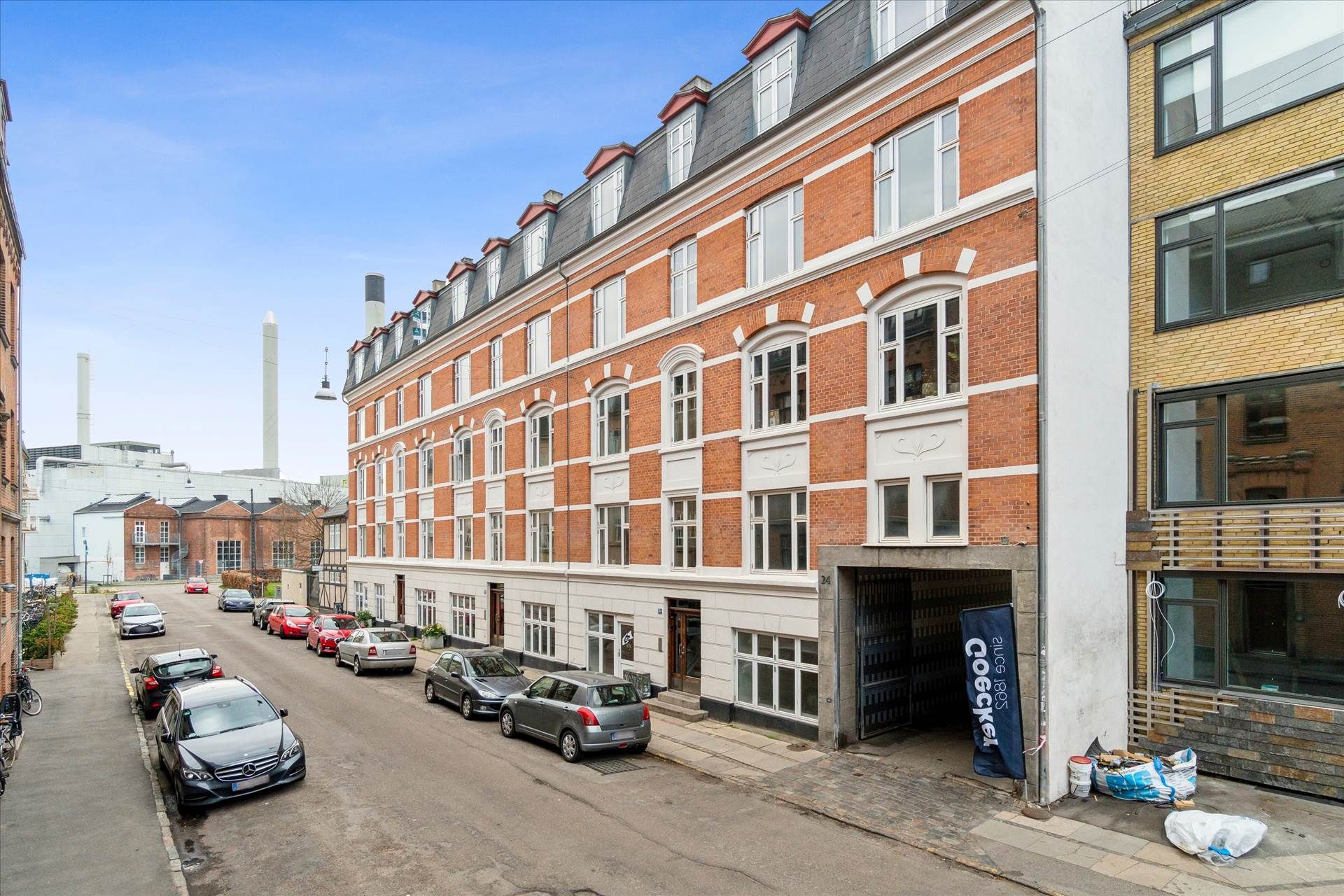 Lejlighed med garage, hvor biler er parkeret og husene er bygget af røde og gule mursten med flere vinduer