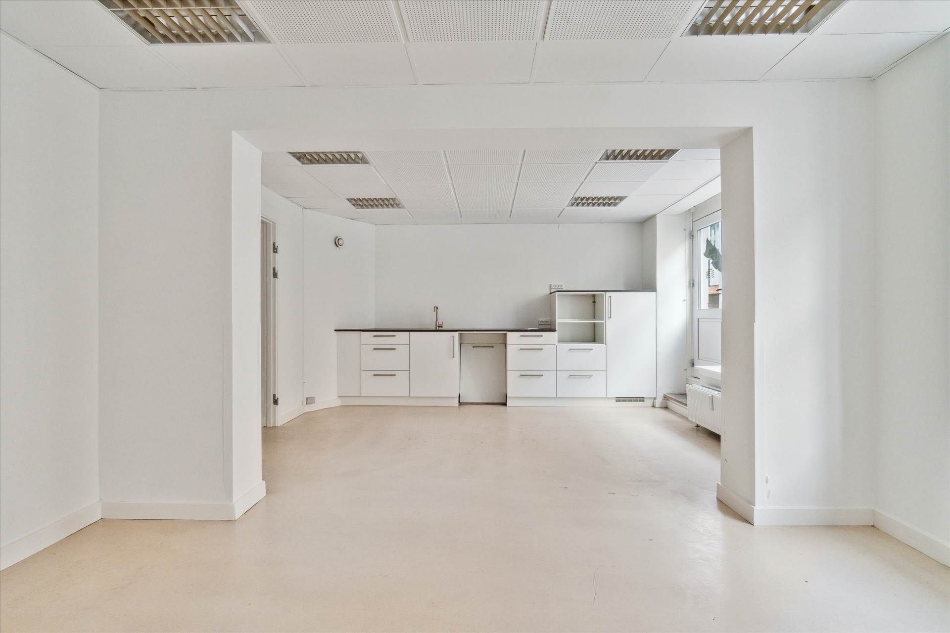 En stor, tom, hvid kontorvirksomhedslokaler med hvide vægge og lofter og en stor åbning til næste rum med vinduesglas og