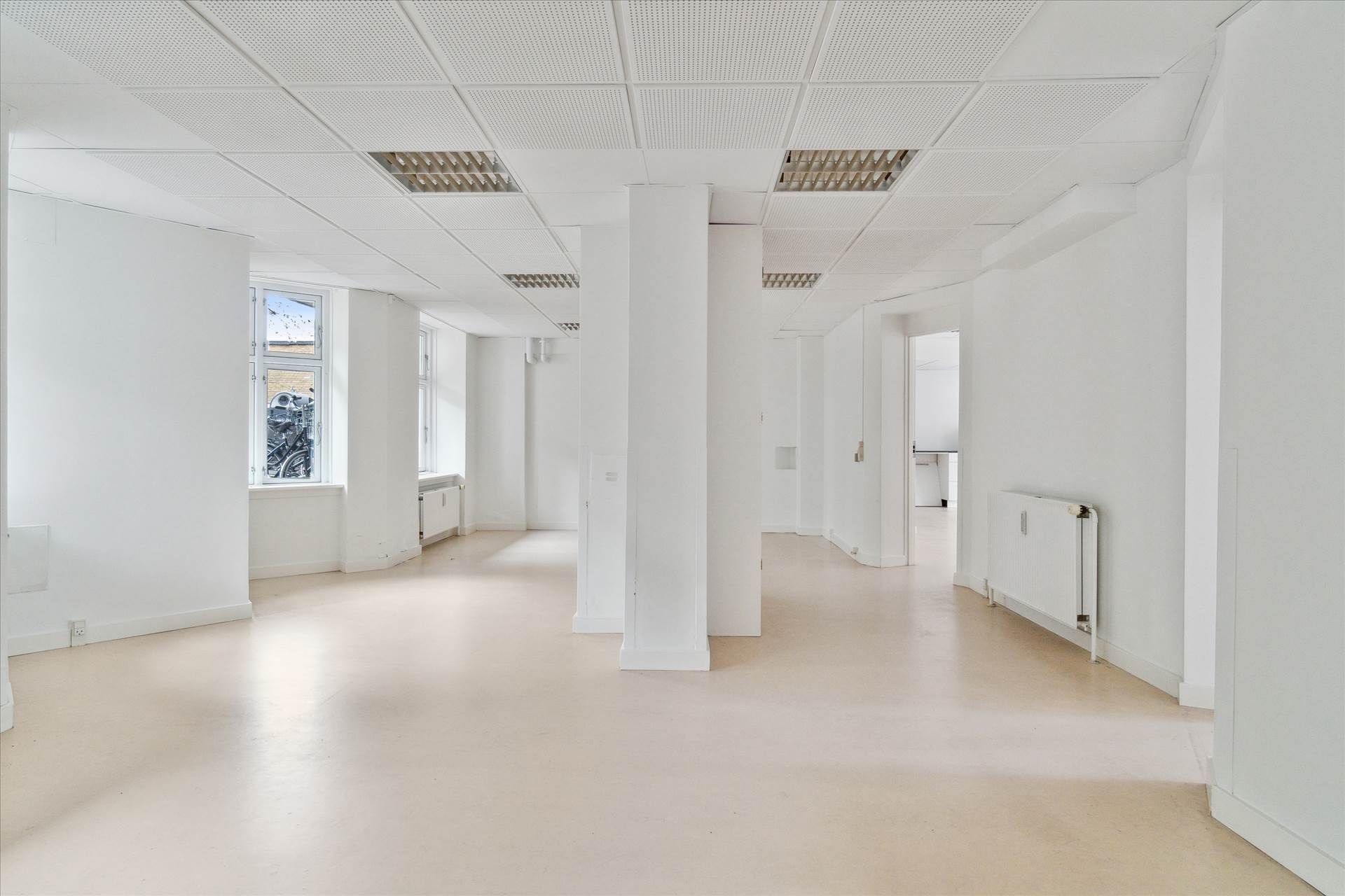 Store, hvide, lyse kontorelokale med en høj og lyse kælder. Væggene er hvide, gulvet er lysegråt og loftet er lavet af hvide