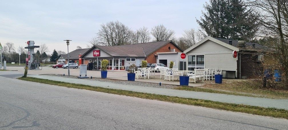 En grillbar med Coca-Cola-skilt og Coca-Cola-reklame. Foran er der hvide stole og borde med blå potter. Der er også en