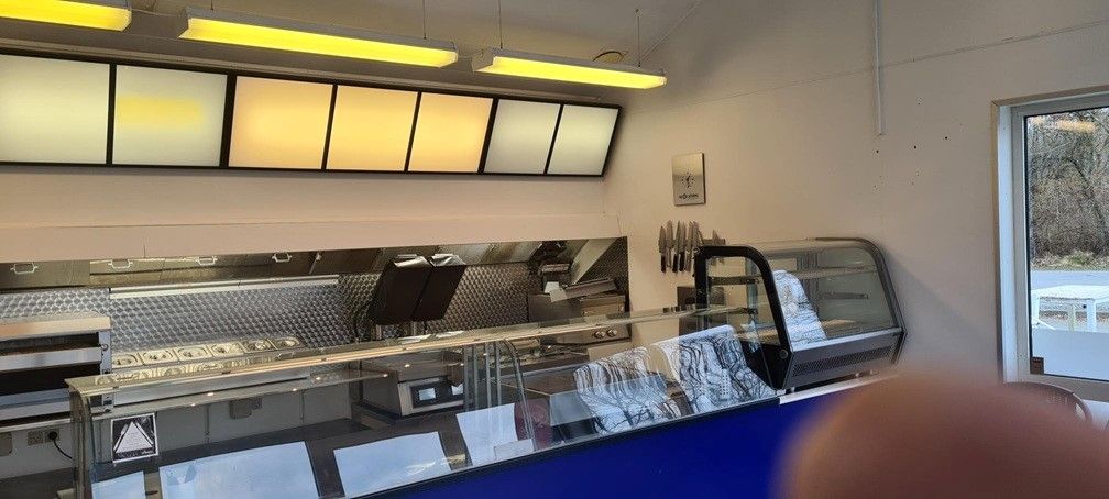 En grillbar med moderne udstyret og lyse gulve og vægge, og et køleskab med glasdør og et udvalg af knive.