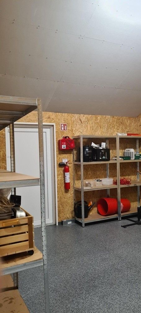 I rummet er der metalhylder med ting som en vandkande, redskaber og røde spande samt et ildslukker og en rødt brandkasse.