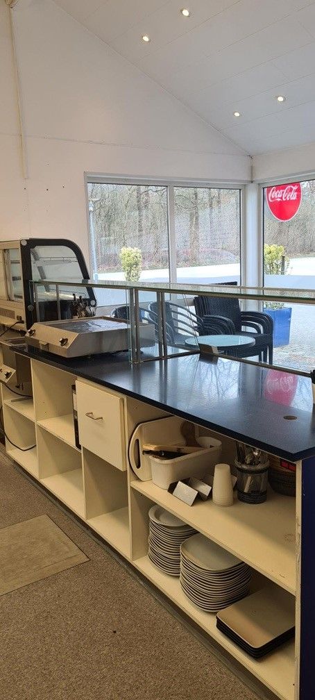 Grillbar med moderne interiør og komplet udstyr til forpagtning. Kontor med glas og møbler samt Coca Cola-logo på vinduet.