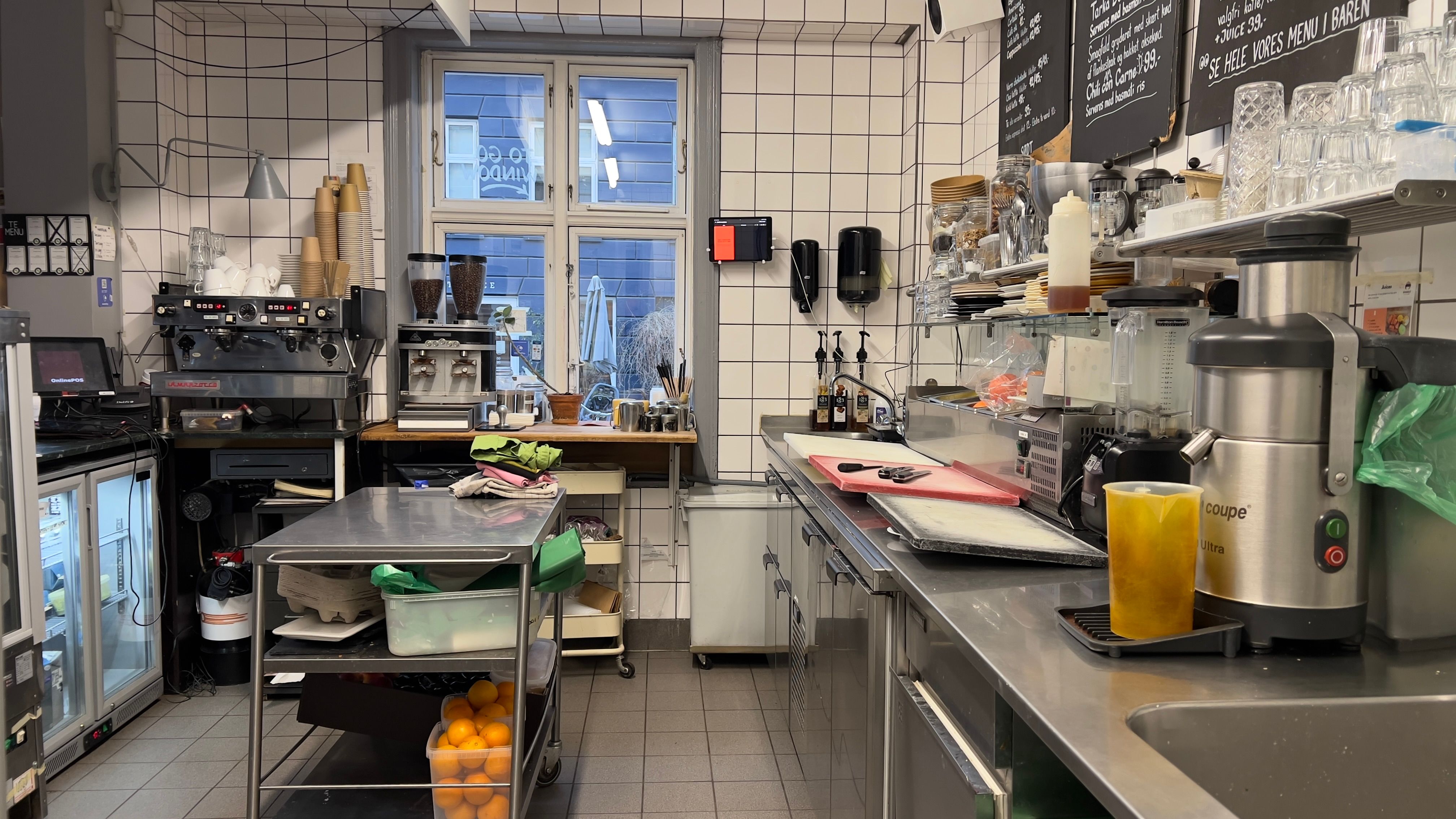 Erhvervslejemål med fuldt indrettet café-køkken med ekspreskaffemaskine, juicemaskine og skåle og glas på hylden. Der er en