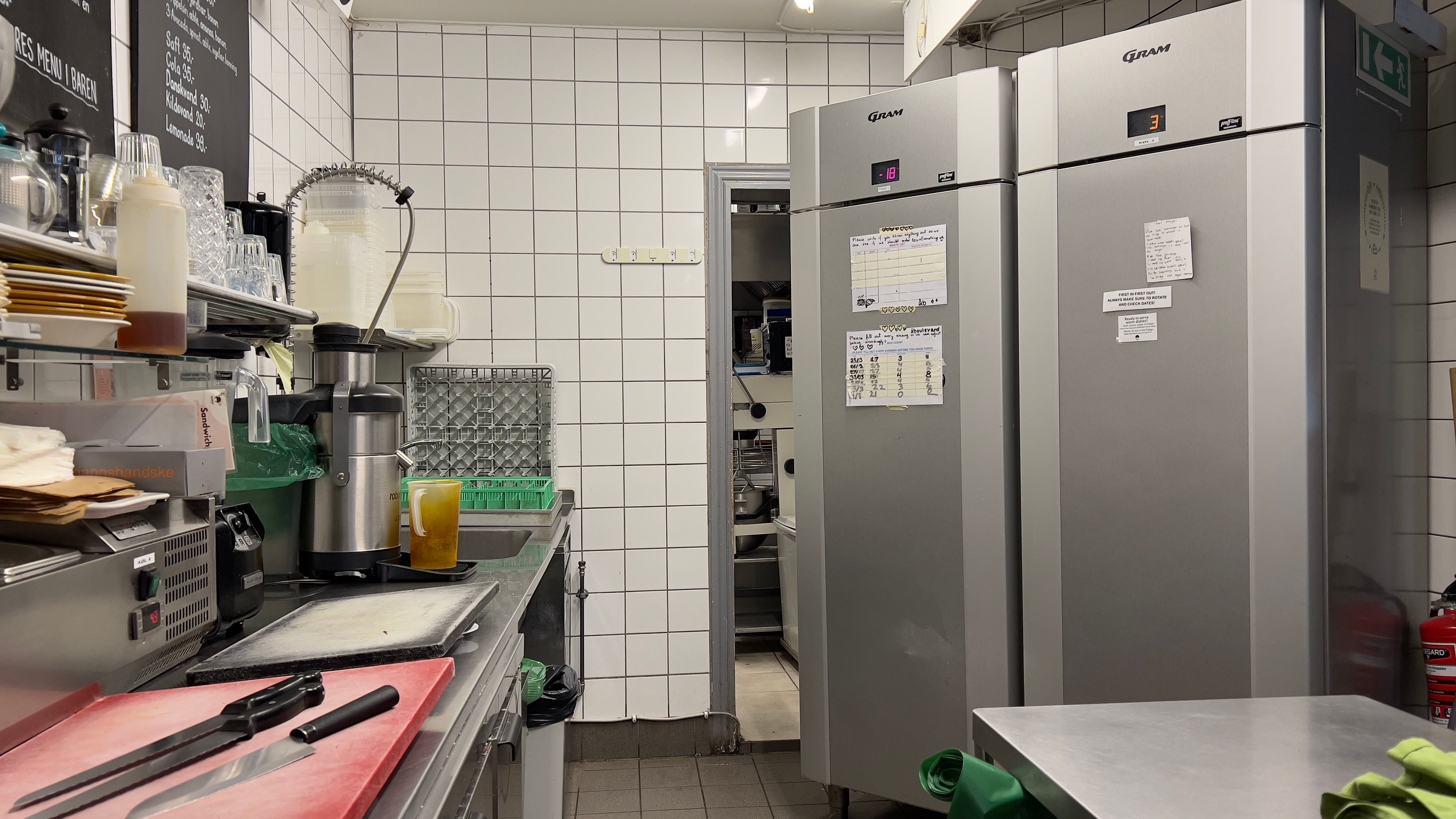 Køkken med to store køleskabe, røde skærebræt, knive, skriveplade og flere apparater