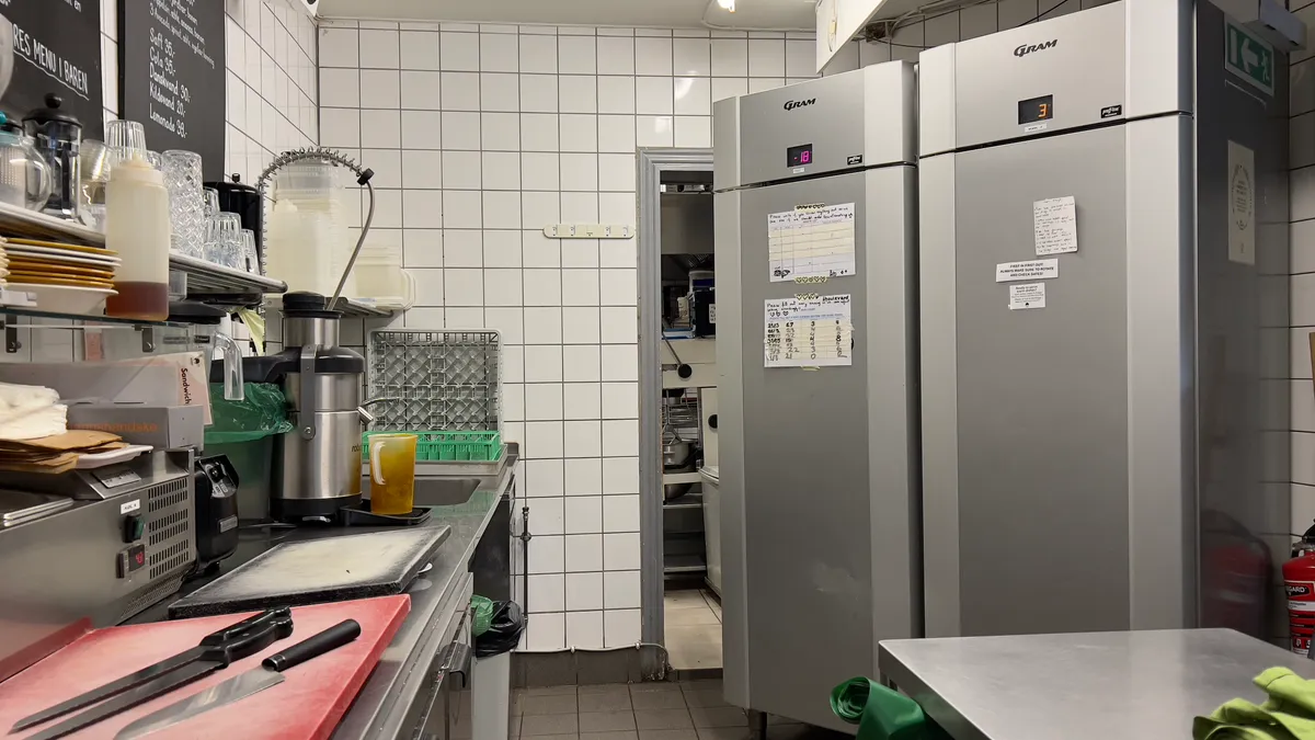 Køkken med to store køleskabe, røde skærebræt, knive, skriveplade og flere apparater