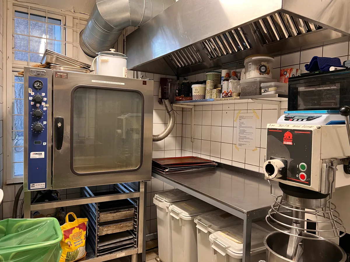 Køkken med komfur, ovn, mikser, afløbsfiltre, hætte og hylder med ingredienser og salt.