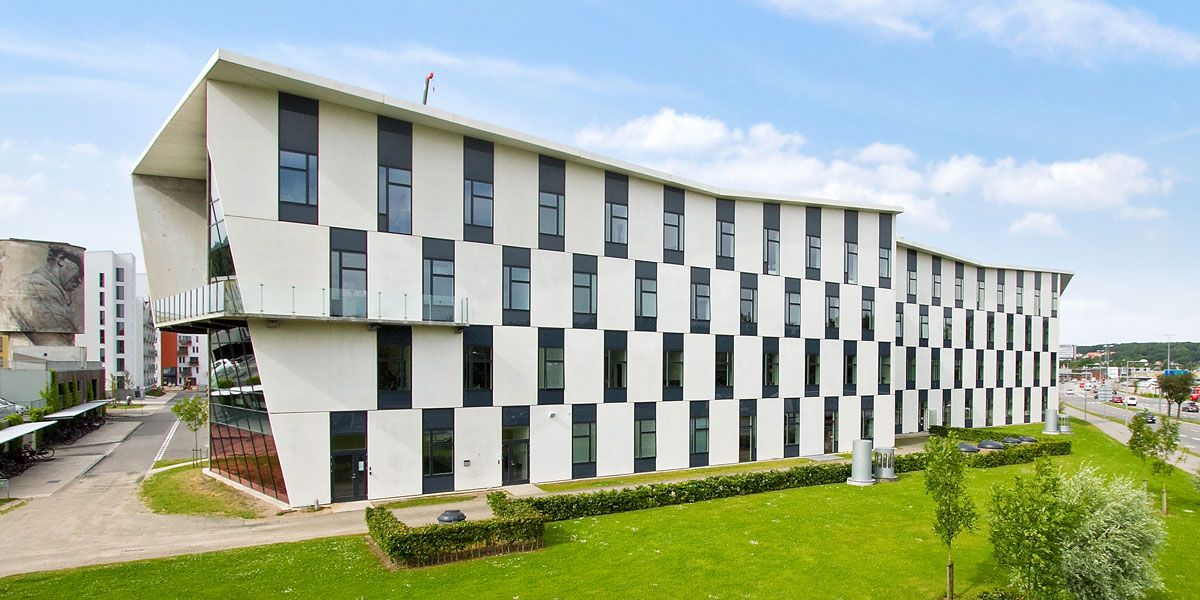 Lyserummelige kontorbygning med lyse, hvide og sorte ruder og udsigt over grønne græsflade med buske og træer