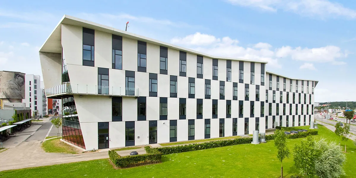 Lyserummelige kontorbygning med lyse, hvide og sorte ruder og udsigt over grønne græsflade med buske og træer