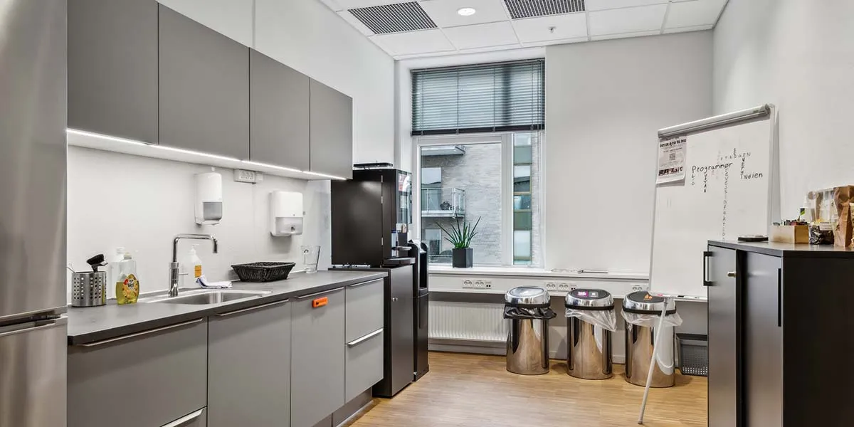 Lyst og moderne kontor med lyse hvide vægge og gulve, en stor hvid tavle og lyse sølvfarvede køleskabe og køkkenudstyr