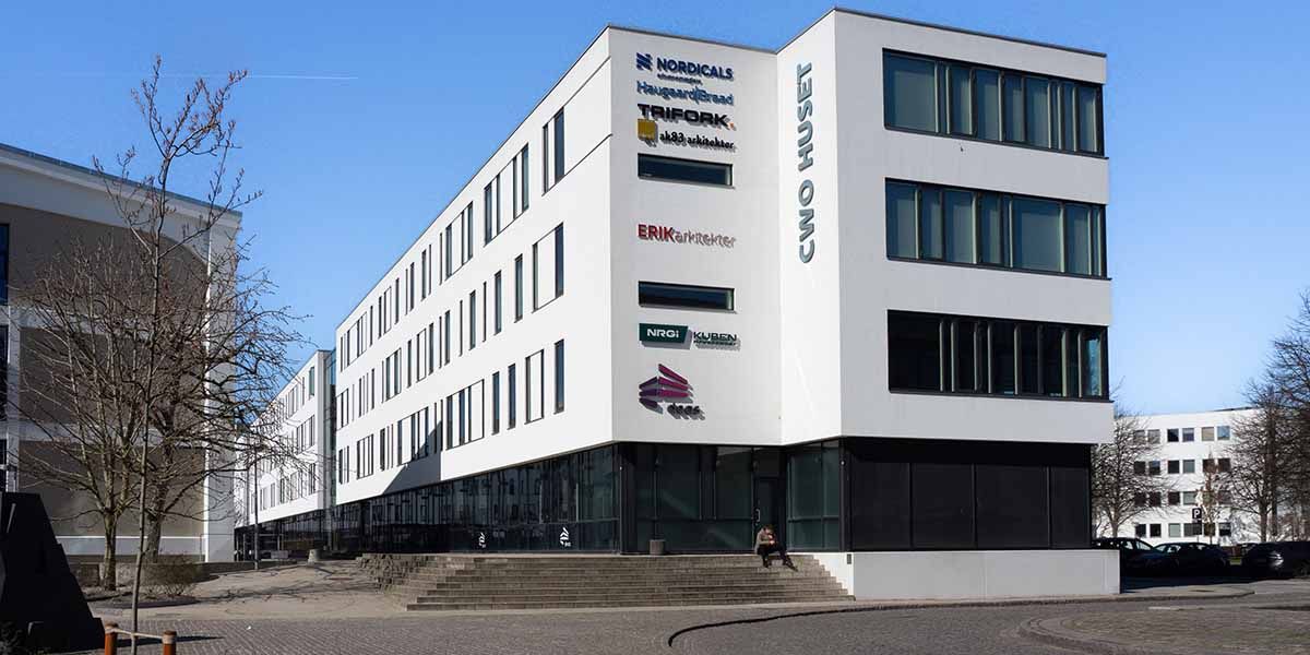 Højhus med glas og hvide facader i Aalborg. Firmaer Nordicals, CWO Huset og flere har skrift på facaden. Stigene og trær