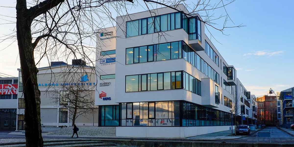 Kontorbygning med glasvinduer og indgang til venstre og en person, der går forbi på gaden