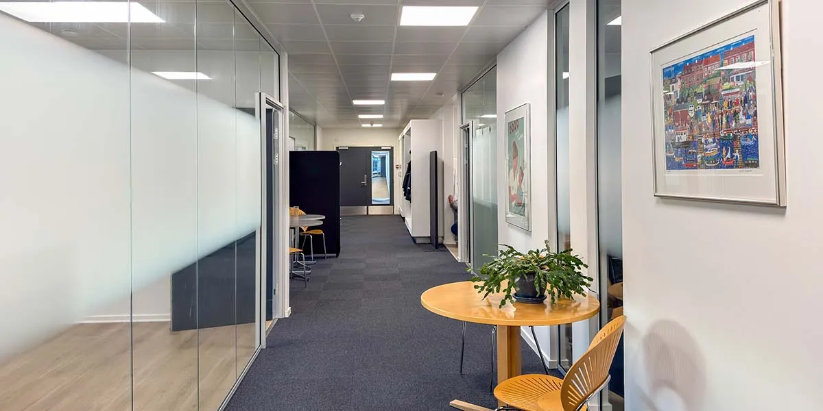 Lejlighedsvise kontorer med moderne interiør. Rundt borde, højttalere og kunstværker på væggen. Glasvinduer og døre giver