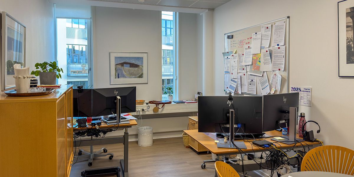 Kontor med moderne møbler og to skriveborde med monitorer, højtalere og diverse teknologi. Væggen er dækket af papirark med