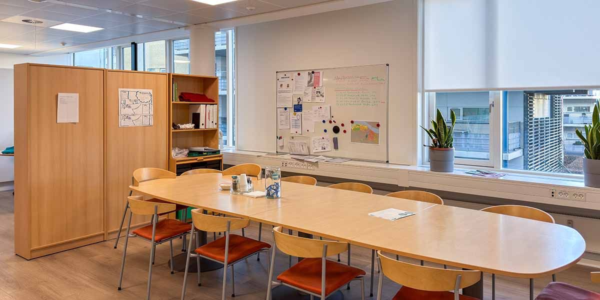 Kontorlokaler med store vinduer og lyse lofter, to store borde, møbelskabe, skriveborde og stolpe.