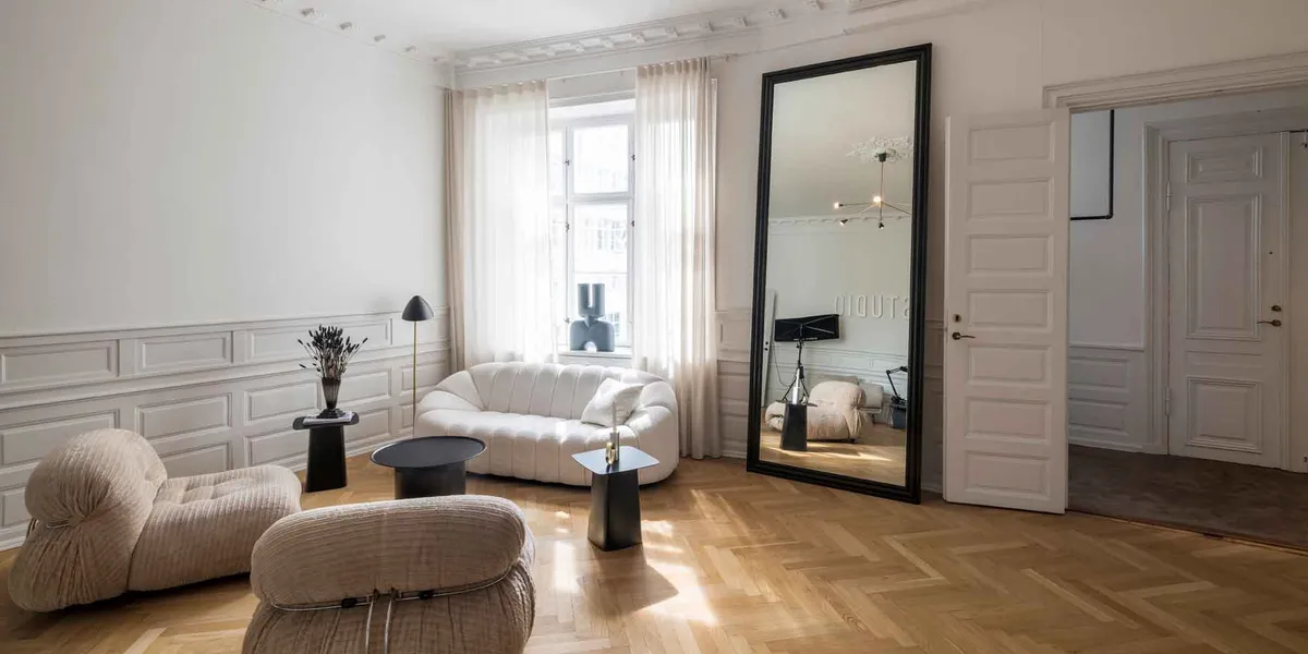 Lejlighed med højloft og moderne møbler og lyse trægulve samt en stor spejl i sort ramme og hvidt vægpanel