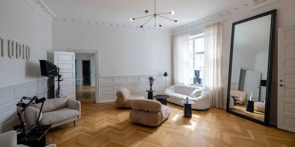 Et moderne interiør med lyse møbler og en stor spejl. Væggene er hvide og gulvet er træ. Et stort hvidt sovesofa med pude.