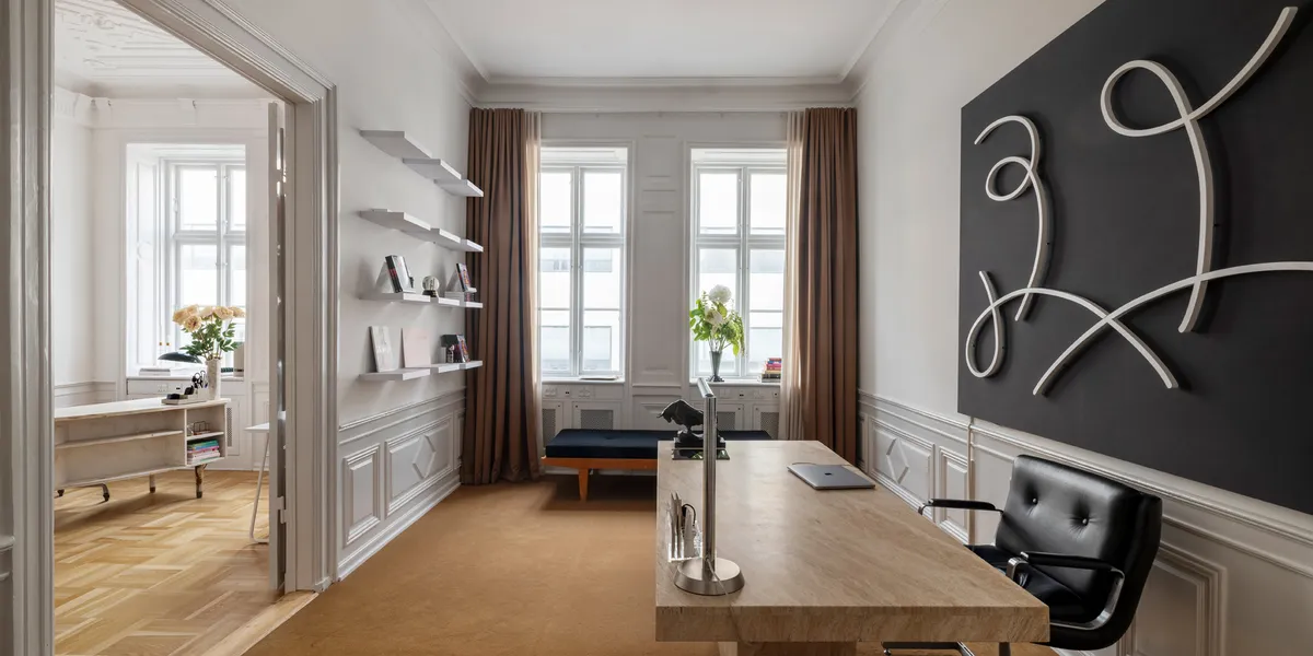 En arbejdsstue med et stort skrivebord og en læder stol samt et værkstedsbord med en bærbar computer og en skulptur