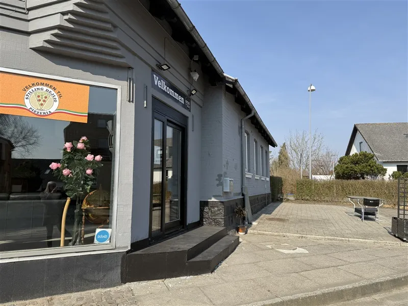 Pizzaria Stilling Deliø, med en velkomstskilt og en blomsterkrans i vinduet, er beliggende i en fredelig bygning med