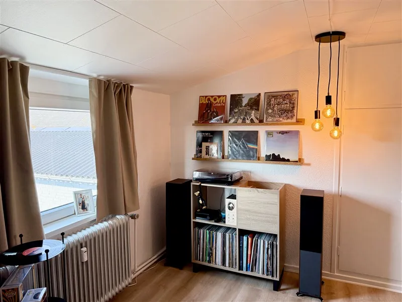 Inde i et værelse med to højtalere, gramofon og cd'er samt en åben vinduesgardin, der viser et udsigt udenfor