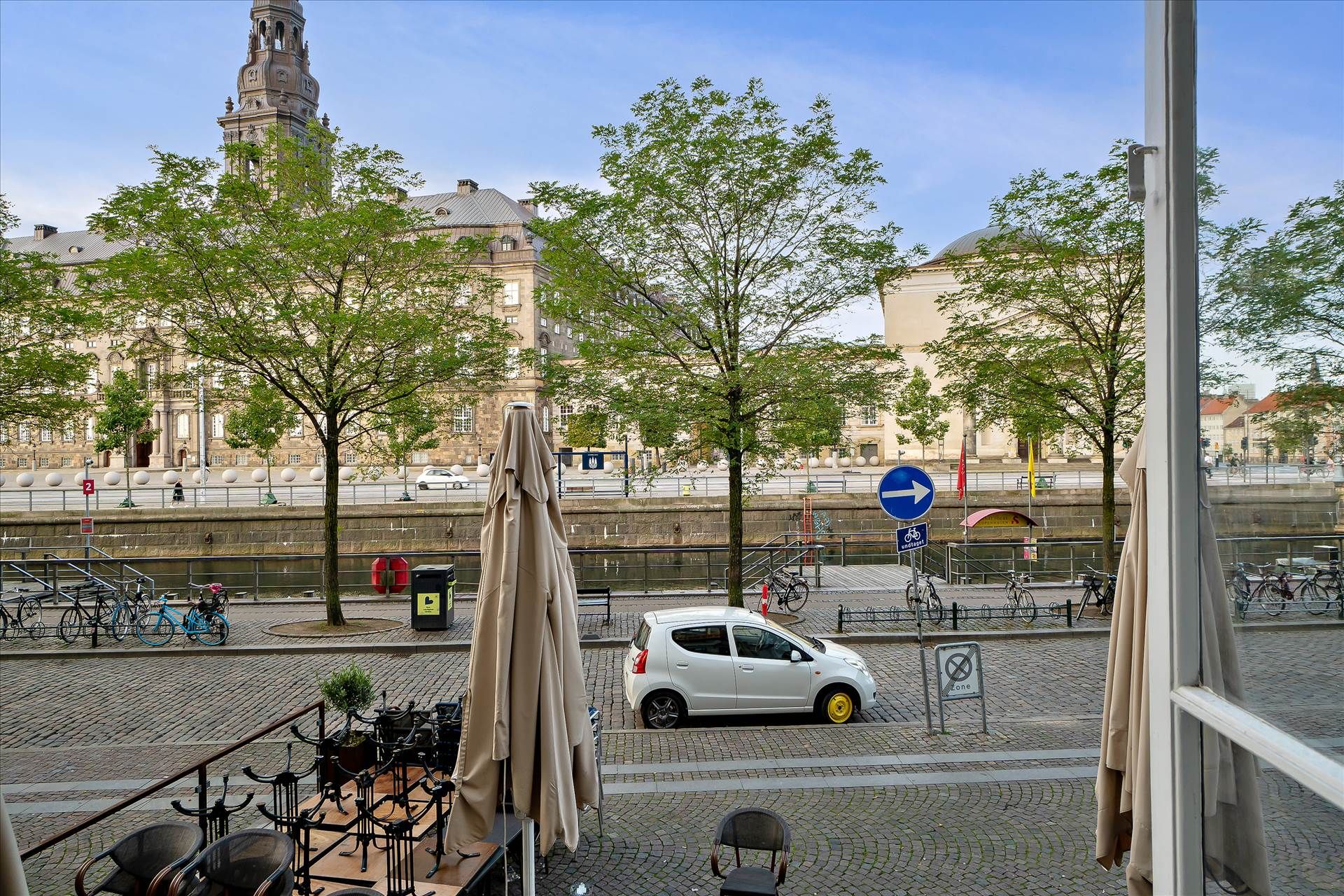 Højtliggende kontor med udsigt over Slotsholmskanalen og Christiansborg Slot. Et lille gult bilkøretøj er parkeret i