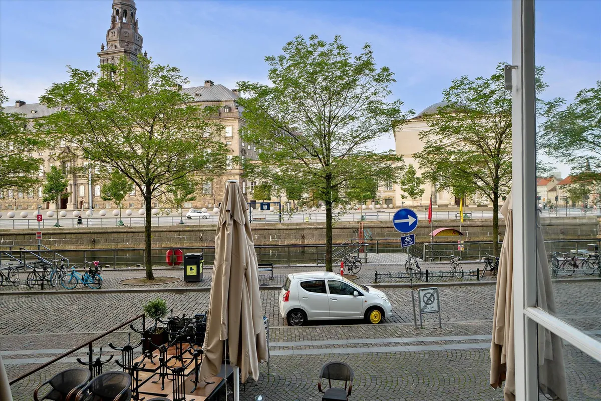 Højtliggende kontor med udsigt over Slotsholmskanalen og Christiansborg Slot. Et lille gult bilkøretøj er parkeret i