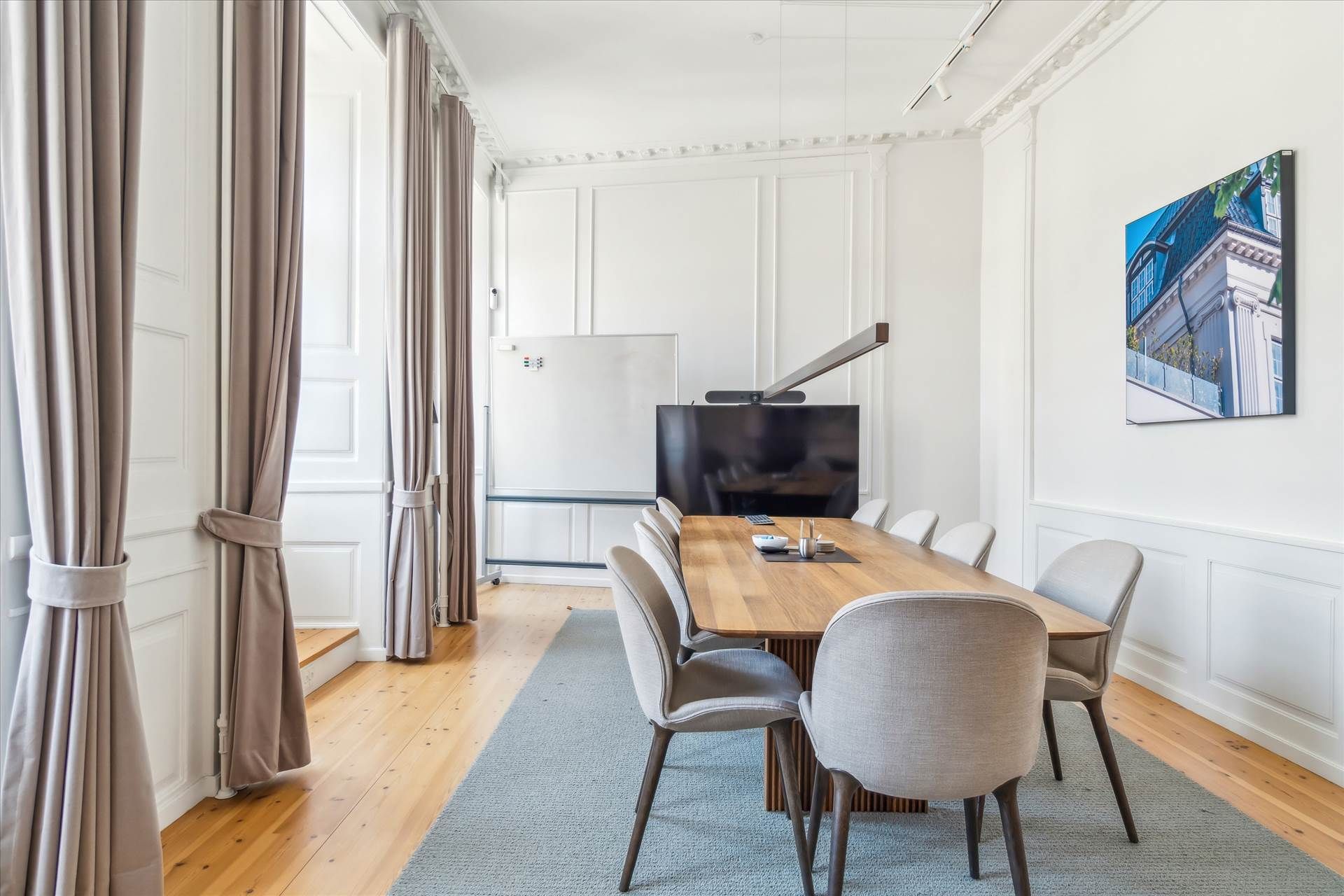 Moderne mødelokale med en lang træbord, høj teknologi og kunst på væggen. Lyse, lysegrå stole med mørkere ben og en stor