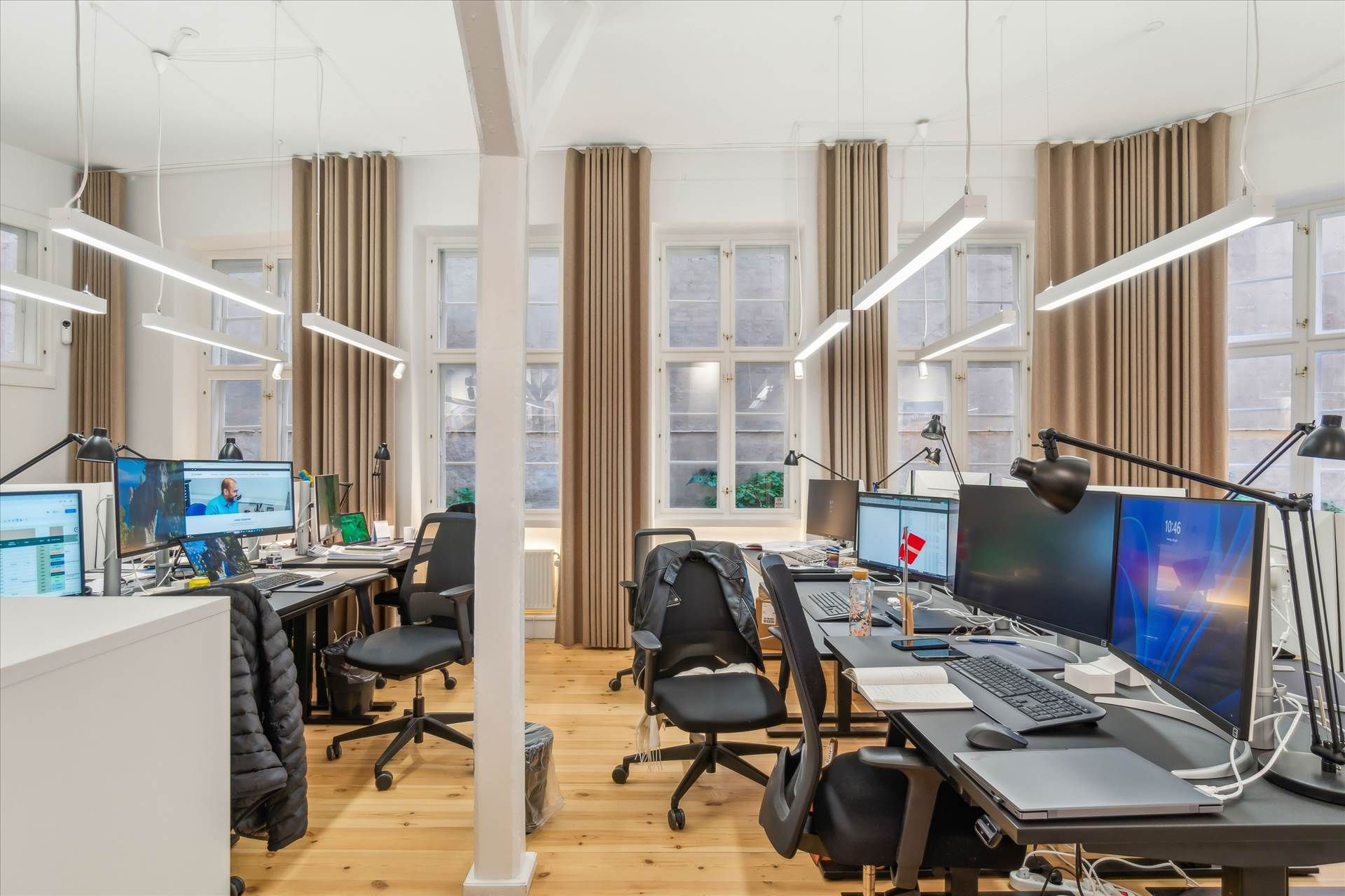 Kontor med lyse lofter og vinduer, lysekroner og højkvalitets skriveborde med computere, stolpe og bukser på stolen og