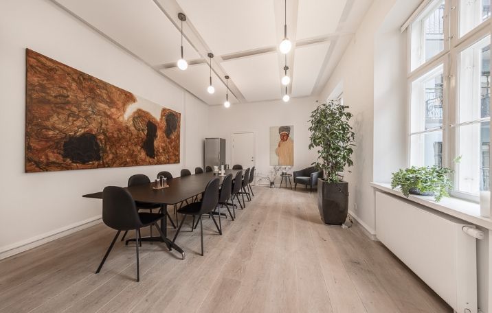 En tom kontorstue med møbler og lysekroner, højloftede lokaler med stuk, høje paneler og vinduer til det lyse udenfor