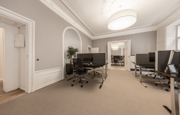 Kontor med højloftede lokaler, høje paneler, stuk og lyse gulve samt computere og stole