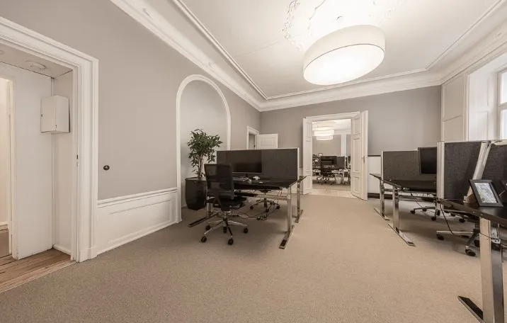 Kontor med højloftede lokaler, høje paneler, stuk og lyse gulve samt computere og stole