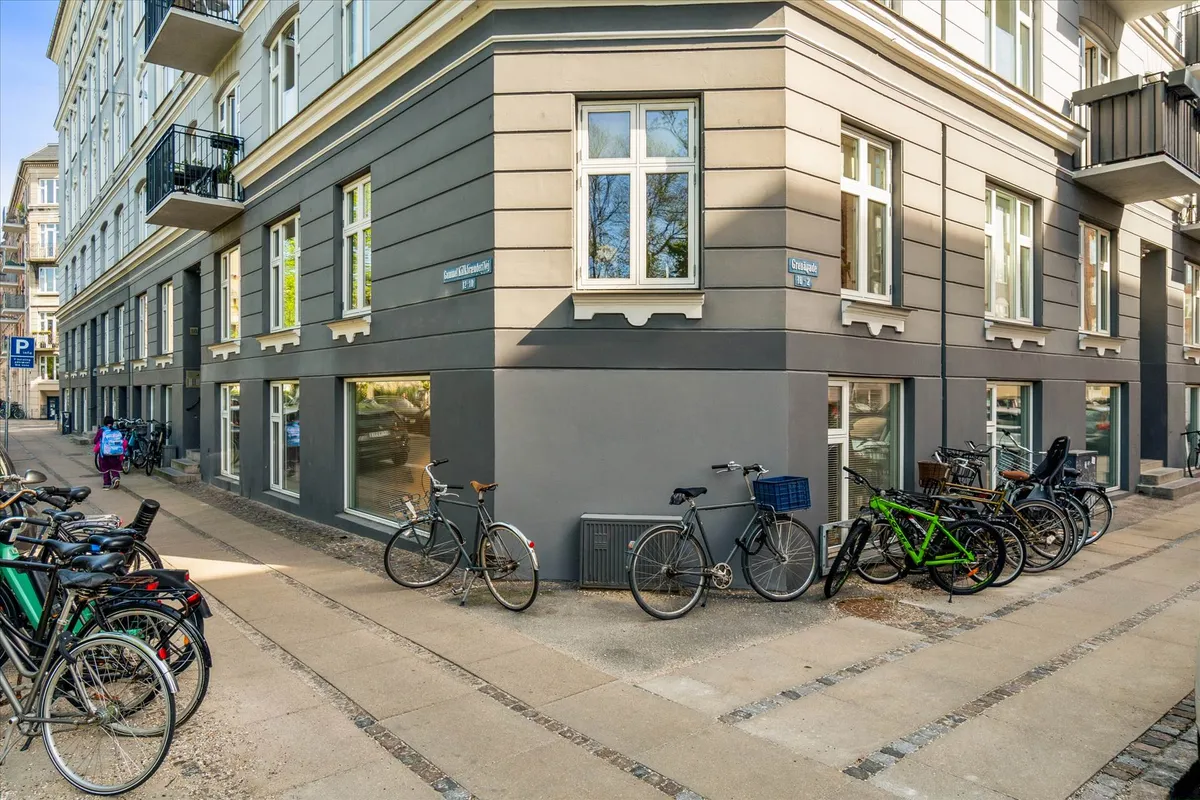 Flere cykler parkeret udenfor et erhvervsbyggeri på Østerbro. En person med rygsæk og en cykel passerer på fortovet.