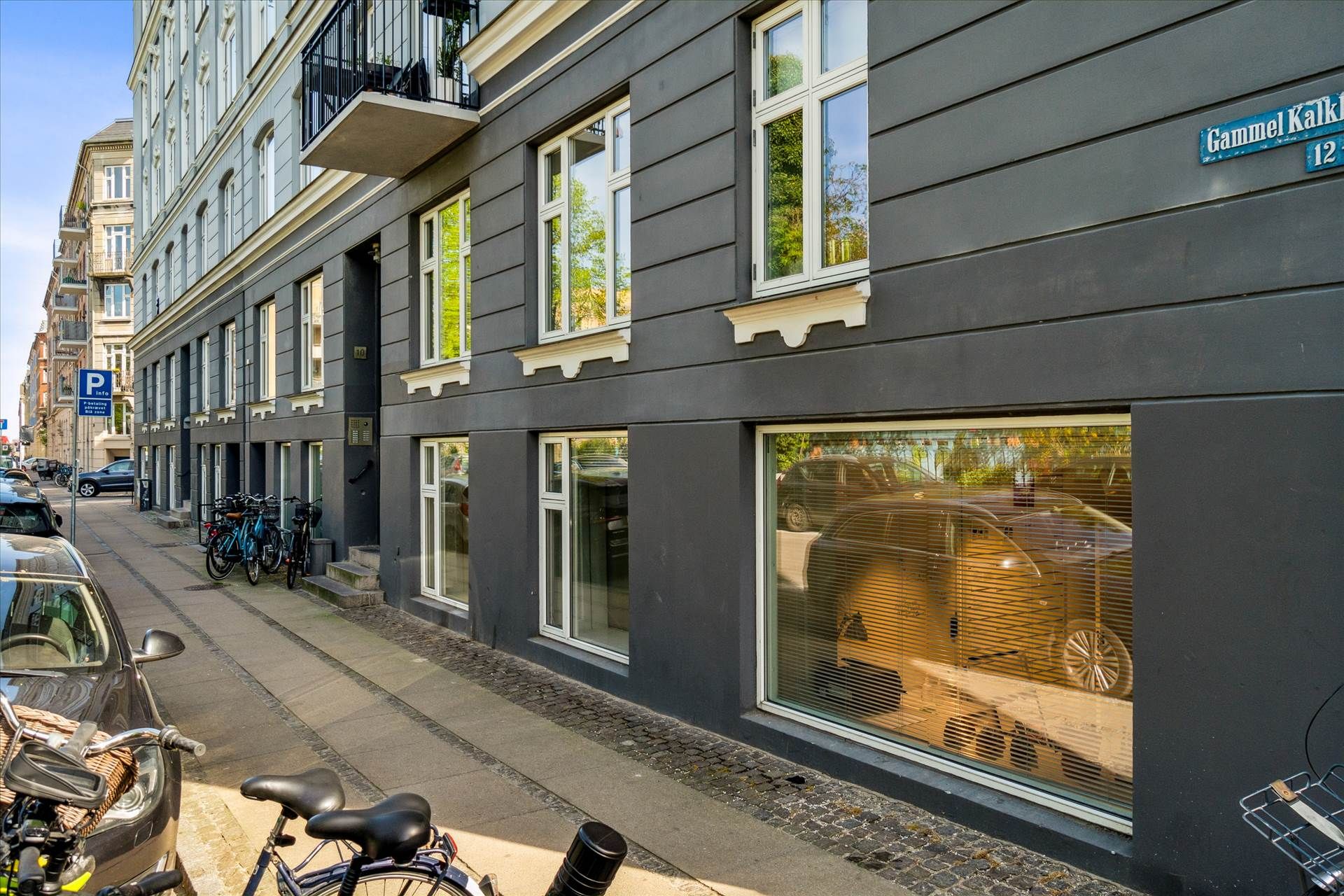 Erhvervsandel med parkeringsplads og cykelstativ ved siden af et byggeværk med adgang til gågade og parkeringsområde