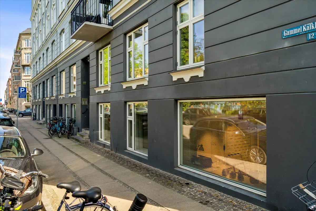Erhvervsandel med parkeringsplads og cykelstativ ved siden af et byggeværk med adgang til gågade og parkeringsområde