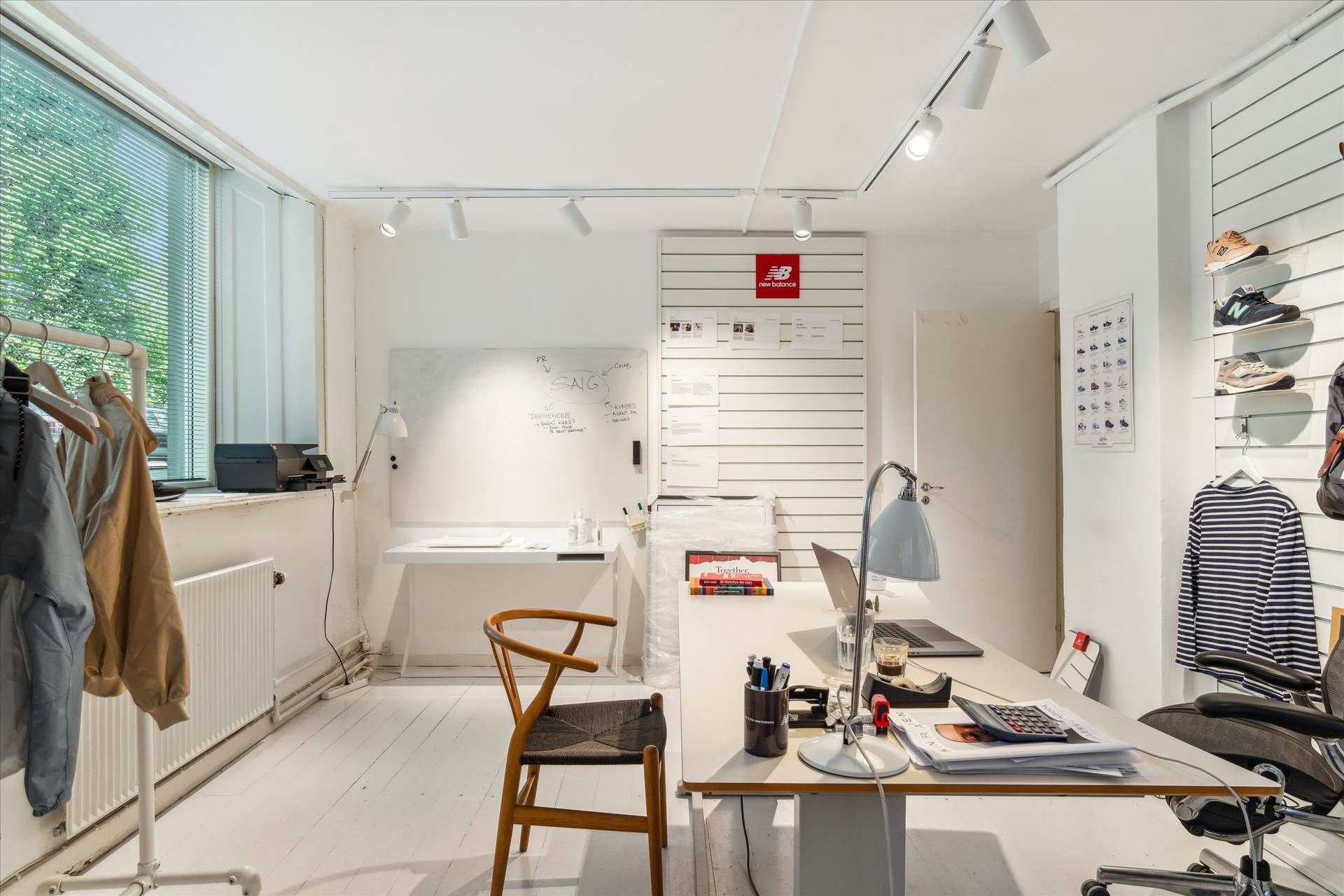 Kontor med to borde, kontormøbler, skrivebordslampe, skrivebordsholder og stol, skrift på væggen og New Balance-sko på hylde