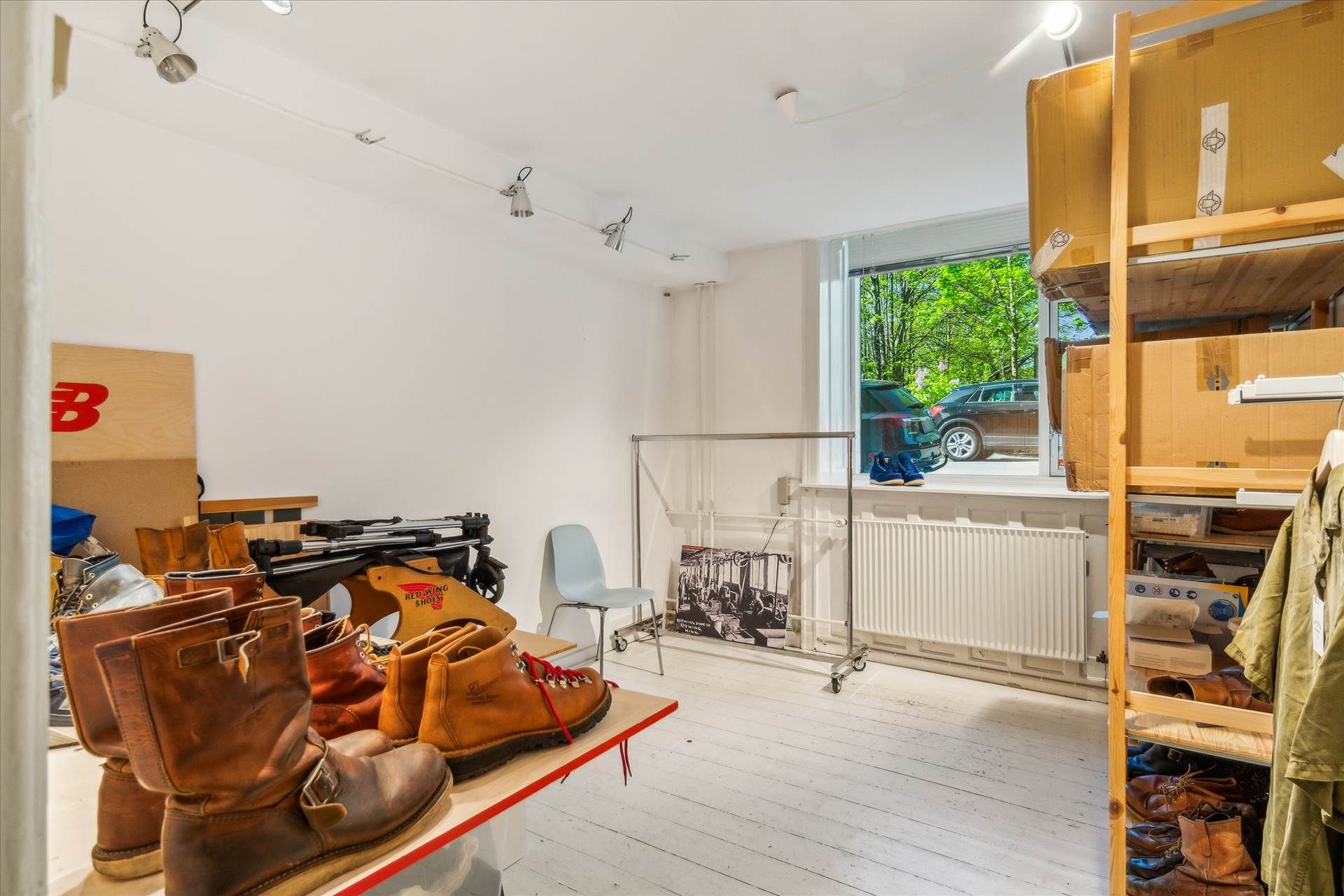 Værelse med højt til loftet, lyse loftslampe, hælstøvler og bøsser på bord og skabe, møbler og udstyr samt udsigt ud til