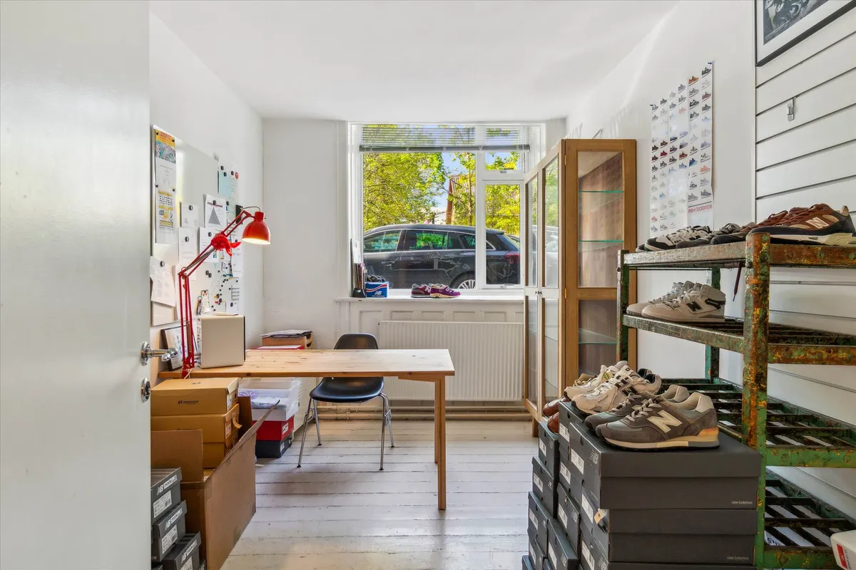 Studieværelse med skrivebord og lampe, skoreoler med New Balance sko, flere kasser med sko og skriftlig information på væggen