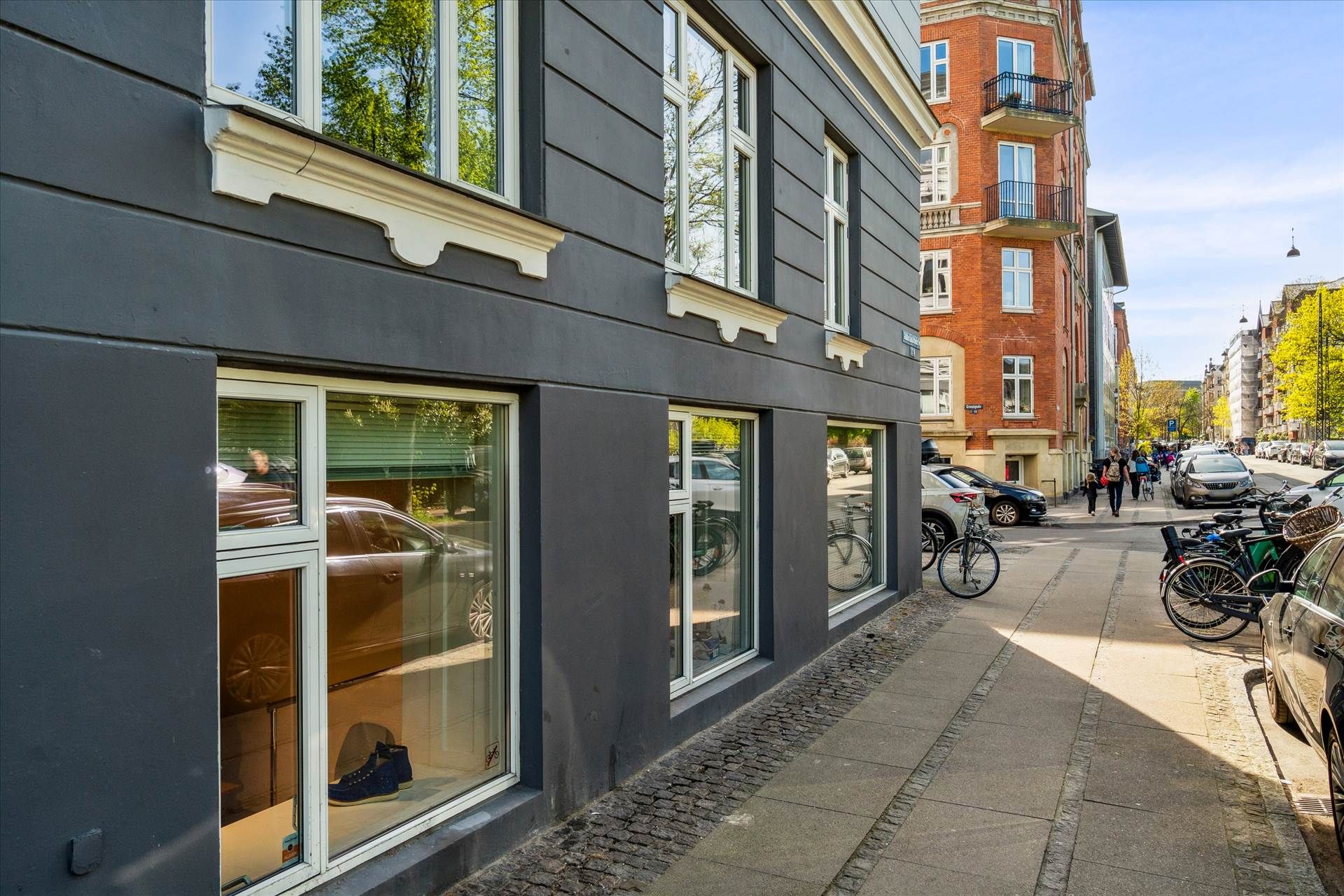 Erhvervslokaler i København med store vinduer og refleksioner af biler og folk. Mange cykler parkeret langs siden af gaden