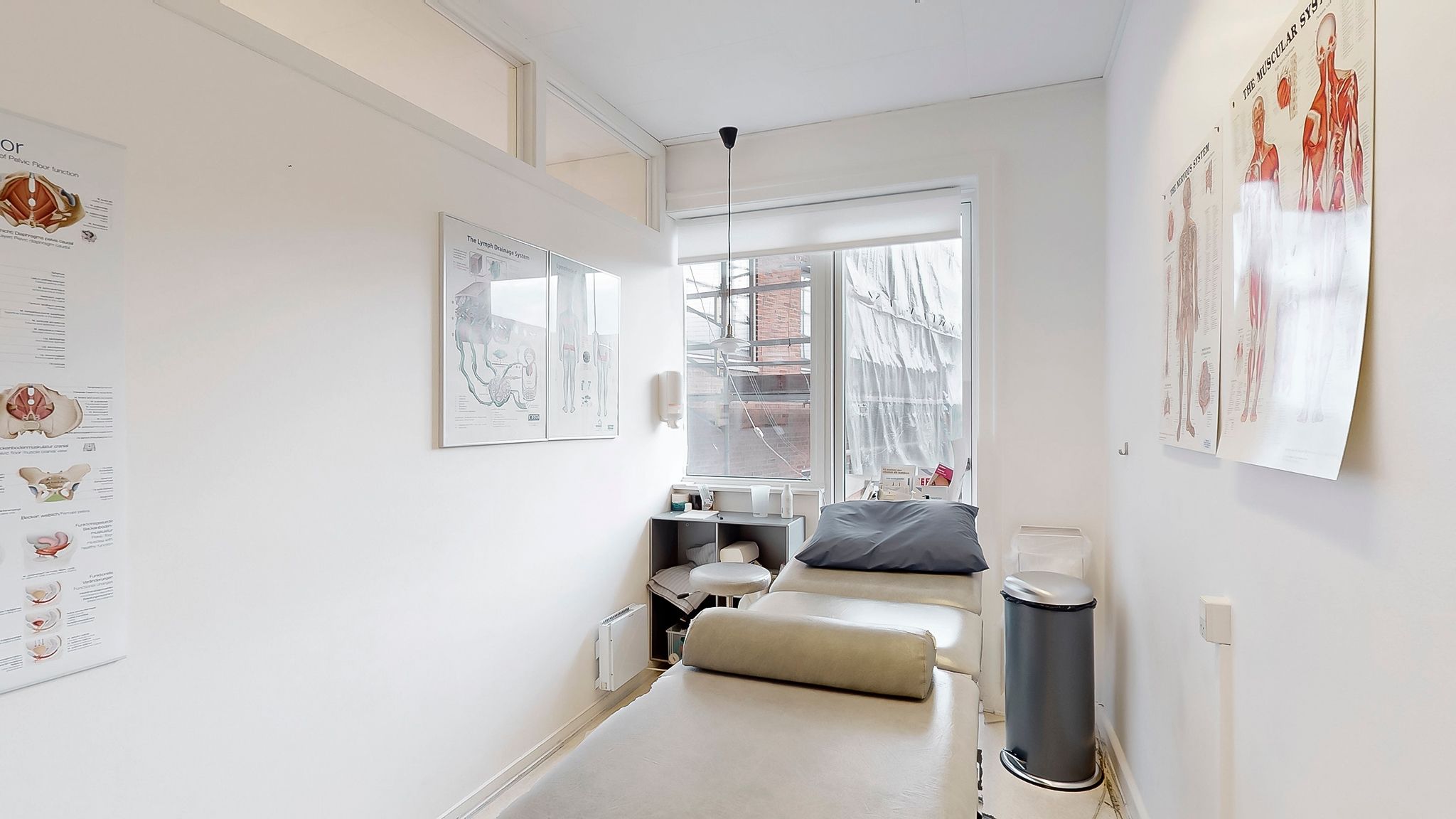 En enkelt lægestol og en massagebord med pude placeret i et funktionelt og rent værelse med hvide vægge og en stor