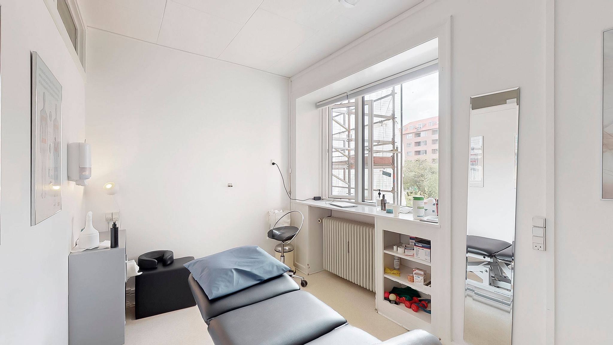 Hvidt og minimalistisk indretning med lægebord og massageseng i en praksis eller klinik. Moderne møbler og udstyr skaber et