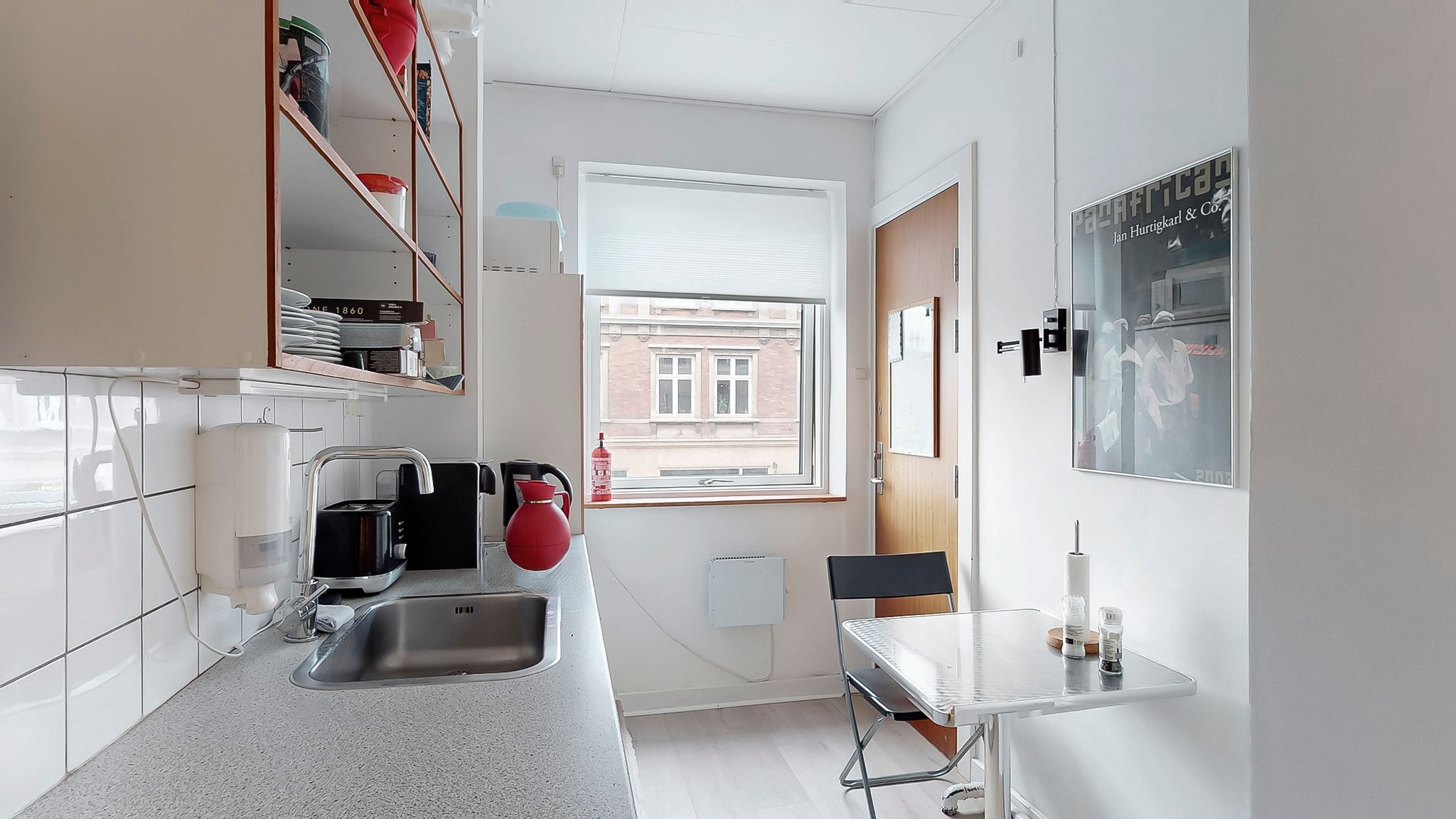 Funktionelt køkken med rustfrit stål, lyse lofter, hvidt gulv og simpel indretning