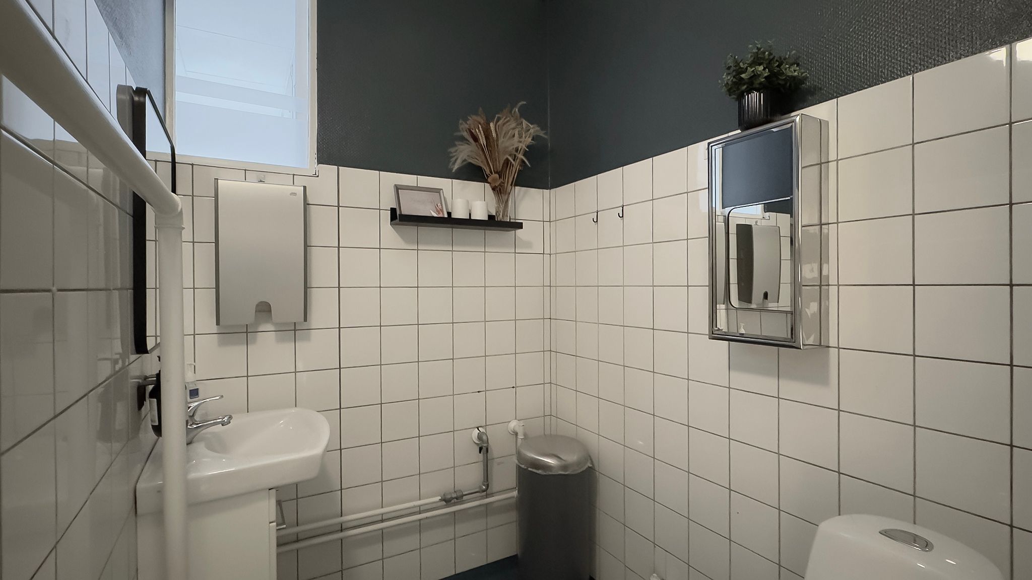 En hvid, funktionel og velplejede toilet med en toiletbørste, håndklædeholder, sæbe og to toiletpapirdispensere samt en
