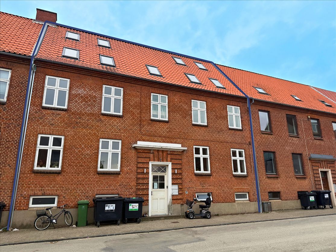 En rækkehus med røde teglsten og hvide vinduerne samt flere skraldespande og en cykel udenfor