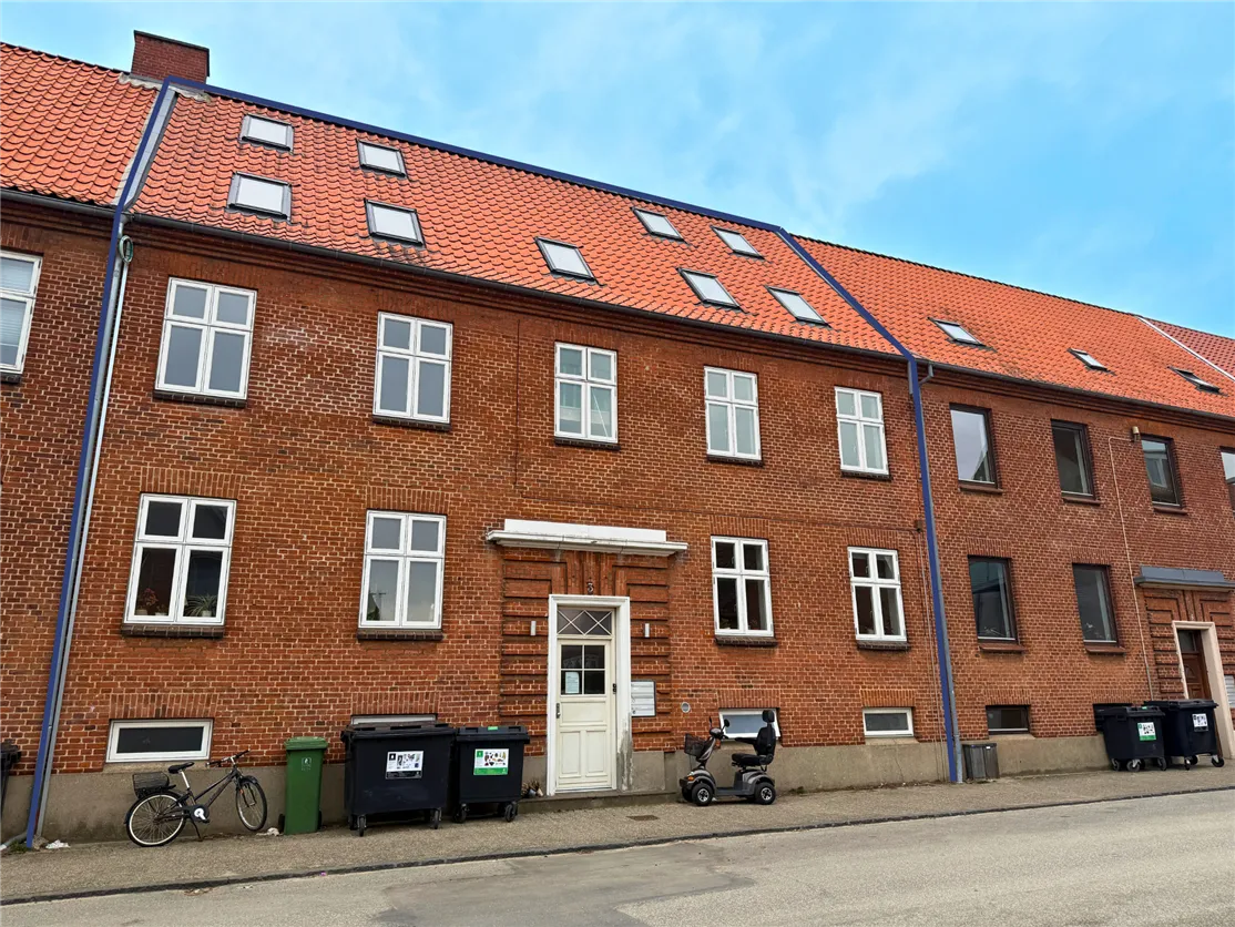 En rækkehus med røde teglsten og hvide vinduerne samt flere skraldespande og en cykel udenfor