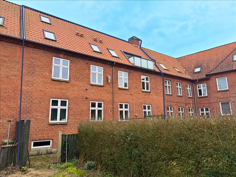 En rækkehuslejlighed med tre soveværelser og udsigt til parken. En stor busk og grønne planter foran.