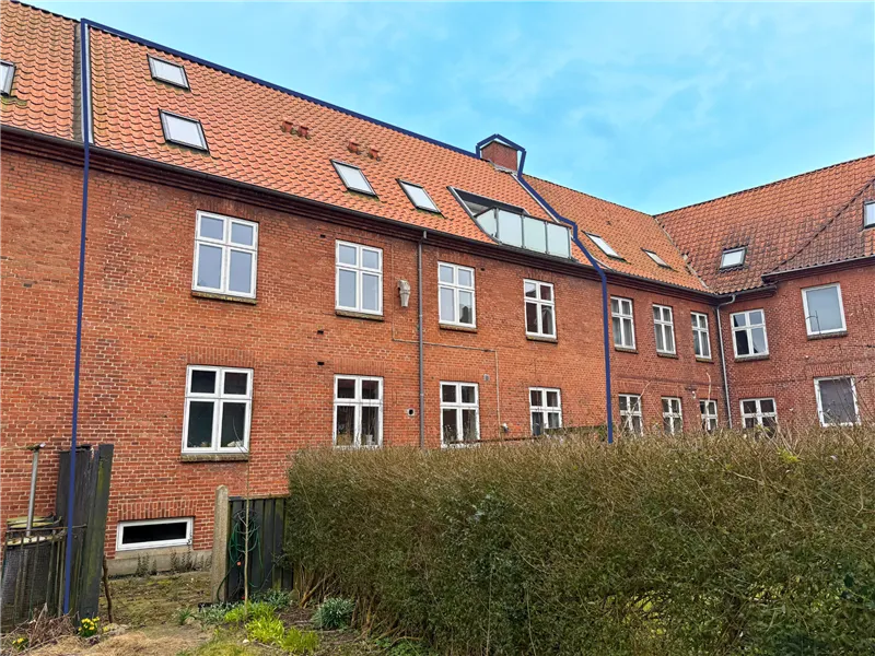 En rækkehuslejlighed med tre soveværelser og udsigt til parken. En stor busk og grønne planter foran.