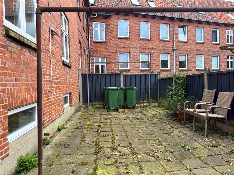 Smuk baghave med lyserøde mursten, to grønne skraldespande, en blomsterpotte og to sæder under et metalrørs stel