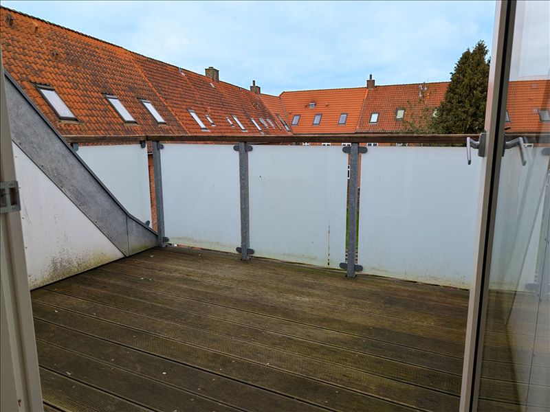 Balkon med udsigt til en række røde tagdækkede huse og et træ i forgrunden