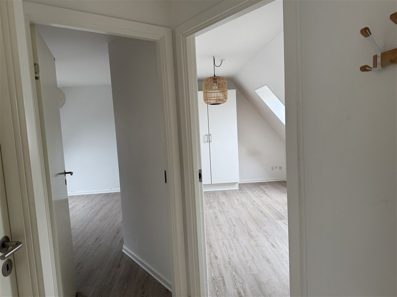 En møbleret lejlighed med åbne døre og hvide vægge, lyse gulve og et bambuslampe i loftet